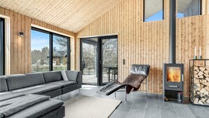A modern interior with a grey sofa, a leather chair, a fireplace, and wooden walls.