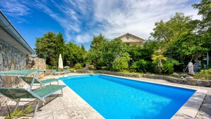 Una piscina rectangular con agua azul cristalina, rodeada por un muro de piedra y abundante vegetación.