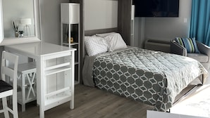 Ett modernt hotellrum med en säng, ett skrivbord med en stol, en TV och ett fönster med gardiner.