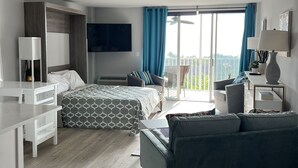 Ett modernt hotellrum med en säng, ett skrivbord, en soffa, en TV och en balkong med utsikt.