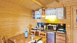Kompakti keittiö, jonka seinät ovat puuta, ja jossa on ruokapöytä sekä peruskeittiövarusteet.