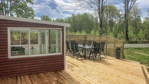 Una terrazza con tavolo e sedie, un piccolo deposito e una finestra che si affaccia su una zona boschiva.
