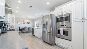 A modern kitchen with stainless steel appliances, white cabinetry, and a granite countertop. - 5BR/3BA NEW Game Room, Pool + Arcade + Fire Pit! (Henderson)
