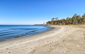 A sandy beach with footprints, a clear blue sky, and a line of trees in the background. - Beautiful home in Löderup with kitchen (Löderup)