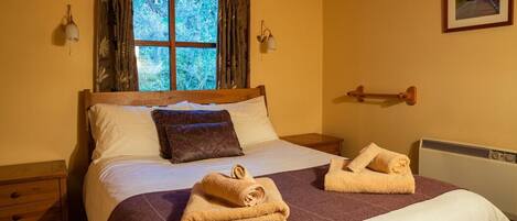A cozy bedroom with a wooden bed, a window with curtains, a bedside table, and a radiator.