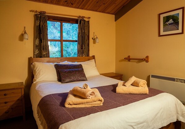 Un dormitorio acogedor con una cama de madera, una ventana con cortinas, una mesita de noche y un radiador.