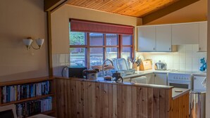 Eine kleine Küche mit Holzvertäfelung, einem Fenster mit rotem Rollo, weißen Schränken und einem eingebauten Backofen.