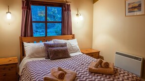 Ein ordentlich bezogenes Bett mit einem gemusterten Überwurf und Kissen, ein Fenster mit Vorhängen und ein Heizkörper an der Wand.