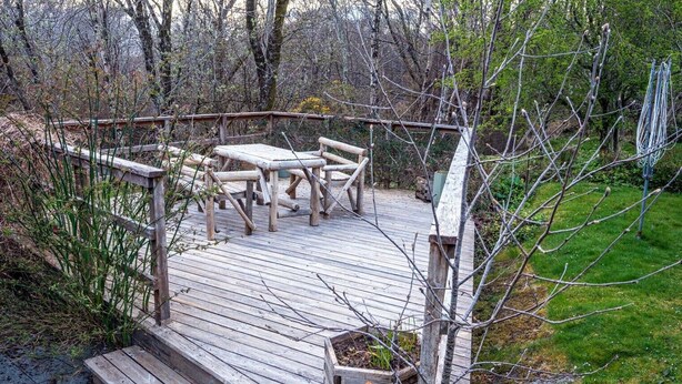 Eine Holzdar Terrasse mit Tisch und Stühlen, umgeben von einem Holzzaun, inmitten eines bewaldeten Gebiets.