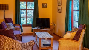 Ein gemütliches Wohnzimmer mit Rattanmöbeln, einem Fernseher und großen Fenstern mit Vorhängen.