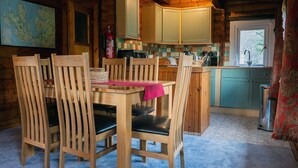 Een houten chaletinterieur met een eettafel en stoelen, een keuken met kastjes en een kaart aan de muur.