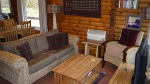 Ein gemütliches Blockhaus-Interieur mit Sofa, Sessel, Couchtisch aus Holz und einem Fernseher.