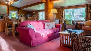 A cozy cabin interior with a pink sofa, wooden furniture, and a large window offering a view of the outdoors.
