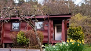 A log cabin with a red exterior, two windows, and a door. - Self-Catering log cabin near Plockton and the Isle of Skye secluded, well equipped and dog friendly. (Kyle)