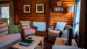 A cozy log cabin interior with two sofas, a coffee table, and a bookshelf. - Self-Catering log cabin near Plockton and the Isle of Skye secluded, well equipped and dog friendly. (Kyle)