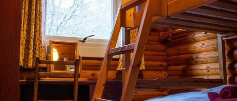 A bunk bed room with a wooden ladder, a desk with a chair, and a window with curtains.