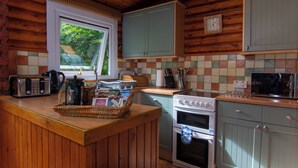 Een houten keuken in een vakantiehuisje, met een raam, een broodrooster, een waterkoker, een fornuis en kastjes.