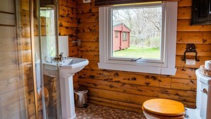 A wooden cabin bathroom with a window, a sink, and a toilet.