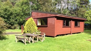 A small red cabin with a picnic table and a green bush in front.
