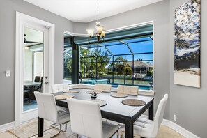 Enjoy meals in this dining area with a large table and comfortable chairs, surrounded by a beautiful view of the pool and lush greenery.