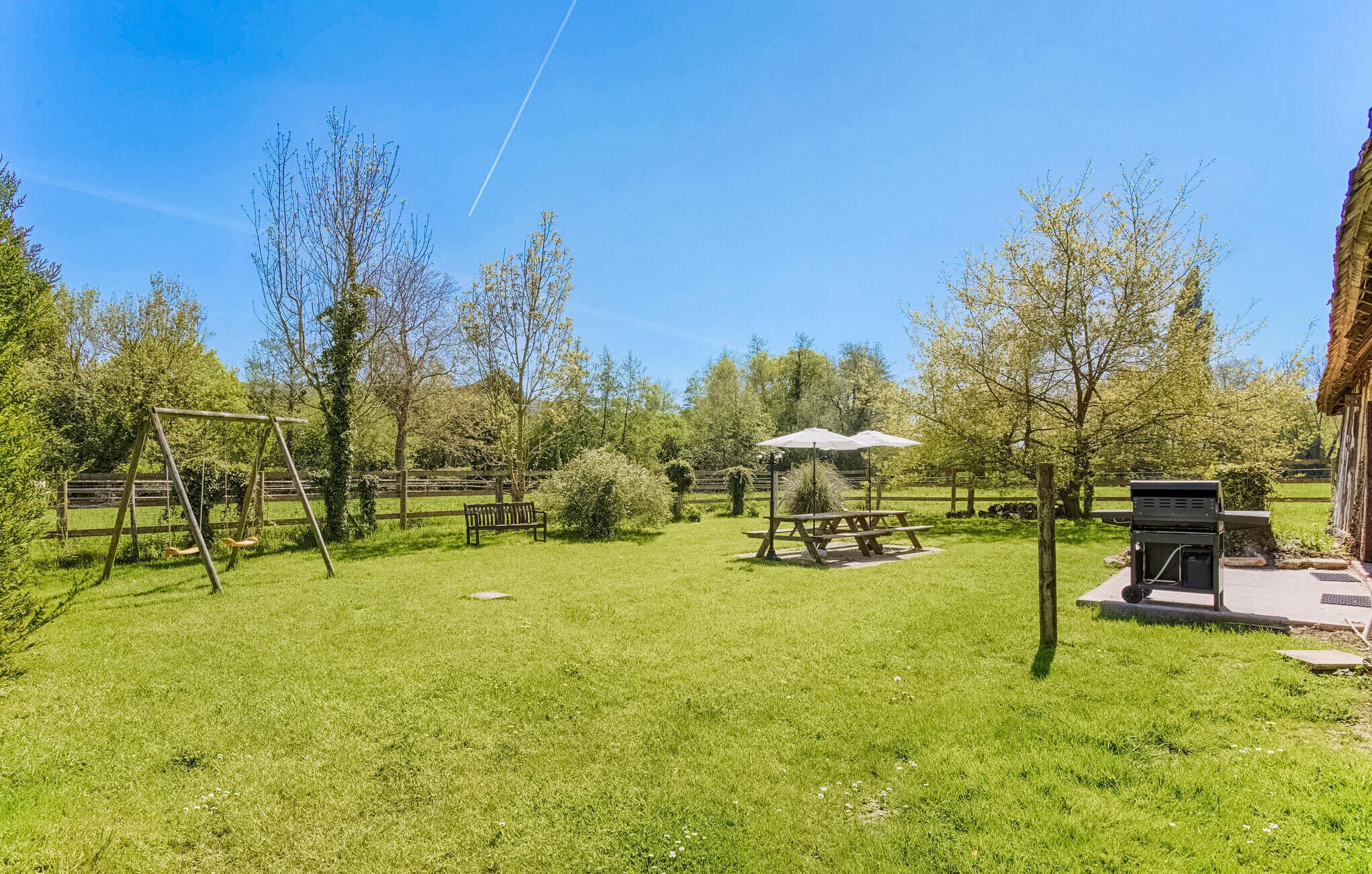 Een gazon met picknicktafels, een schommel en een barbecue.