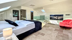 Una moderna camera d'hotel con un letto, un comodino, una sedia rossa e un balcone con ringhiera in vetro.