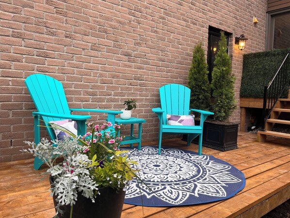 Une terrasse en bois avec deux fauteuils Adirondack turquoise, une table ronde et un pot de fleurs.