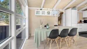 A modern kitchen with white cabinets, a dining area with a table and chairs, and a view of trees through large windows. - 4 bedroom beautiful home in Jerup (Jerup)