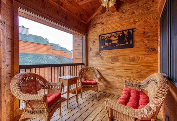 A wooden cabin with wicker furniture and a large window overlooking a mountain.