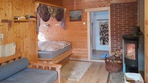 A cozy log cabin room with a bed, a sofa, a fireplace, and a door leading to another room.