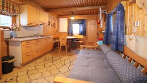 A compact cabin with wooden interiors, a kitchenette, a dining area, and a sofa.