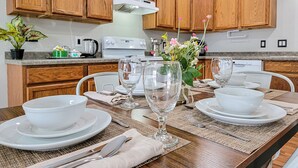 Una cocina moderna con armarios de madera, una estufa blanca y una mesa de comedor preparada para cuatro personas, con copas y platos.