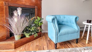 Un sillón azul, una chimenea de madera y una pequeña mesa blanca con una planta.
