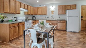 Una cocina moderna con armarios de madera, una mesa de comedor con sillas, un refrigerador y una cafetera.