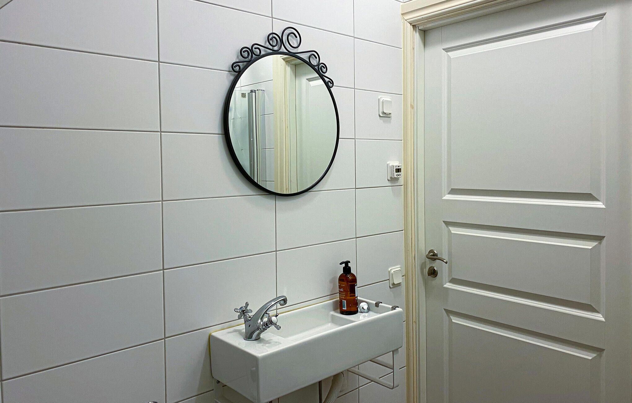 Un baño con un lavabo blanco, un espejo redondo con marco decorativo y una puerta blanca.