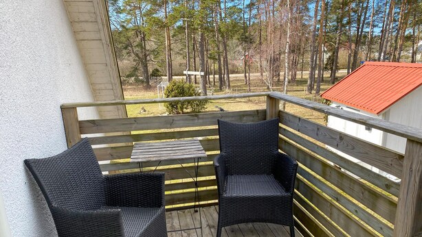 Eine Holzterrasse mit zwei schwarzen Korbstühlen und einem kleinen Tisch.