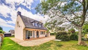 Une maison à deux étages, avec des fondations en pierre, un toit en pente et une véranda à l’avant.