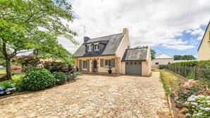 Une allée pavée de pierres menant à une maison dotée d’un toit en pente et d’un petit garage attenant.