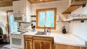 A kitchen with wooden cabinets, a white countertop, a stove, a microwave, and a window with a view of trees.
