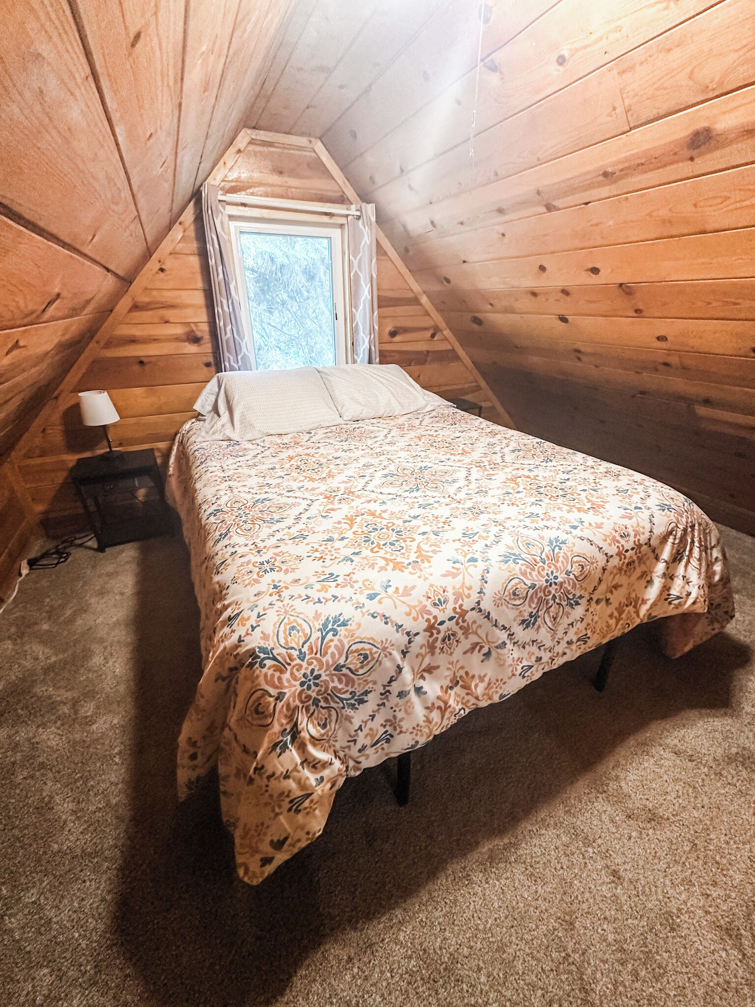 A small, cozy attic bedroom with a single bed, a nightstand, and a window.