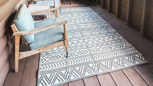 A covered porch with wooden benches and a patterned rug.