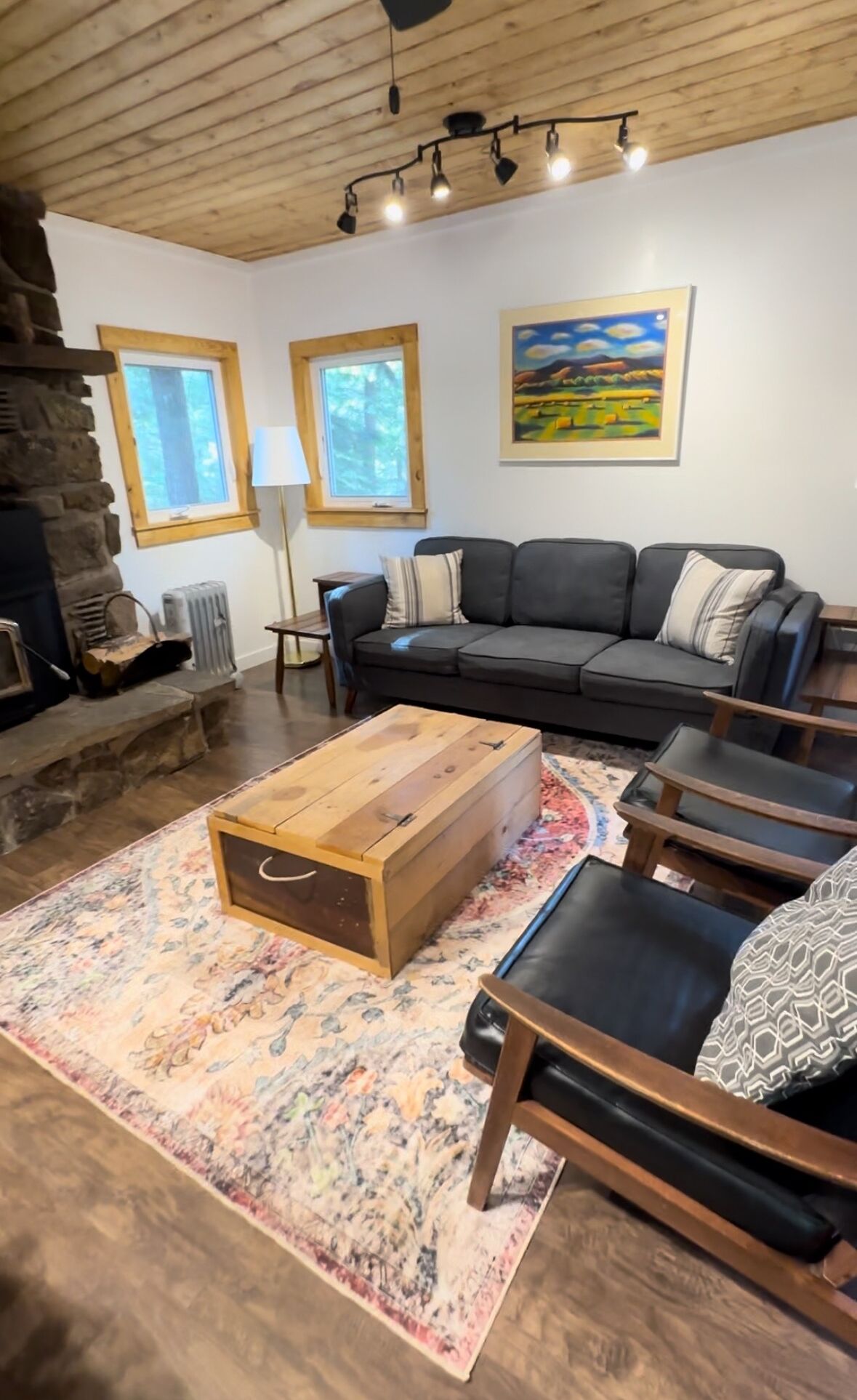 A cozy living room with a stone fireplace, a black sofa, wooden coffee table, and a patterned rug.