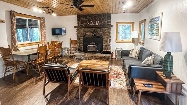 A cozy living room with a stone fireplace, wooden furniture, and a television mounted on the wall.