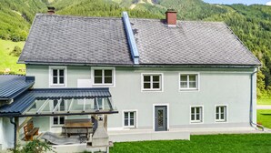 A two-story house with a sloped roof, a front porch with a bench, and a small outdoor grill. - Ferienwohnung in Vordernberg (Vodernberg)