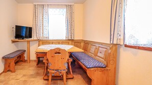 A room with a wooden table, two benches, a television on a stand, and a window with curtains. - Ferienwohnung in Vordernberg (Vodernberg)