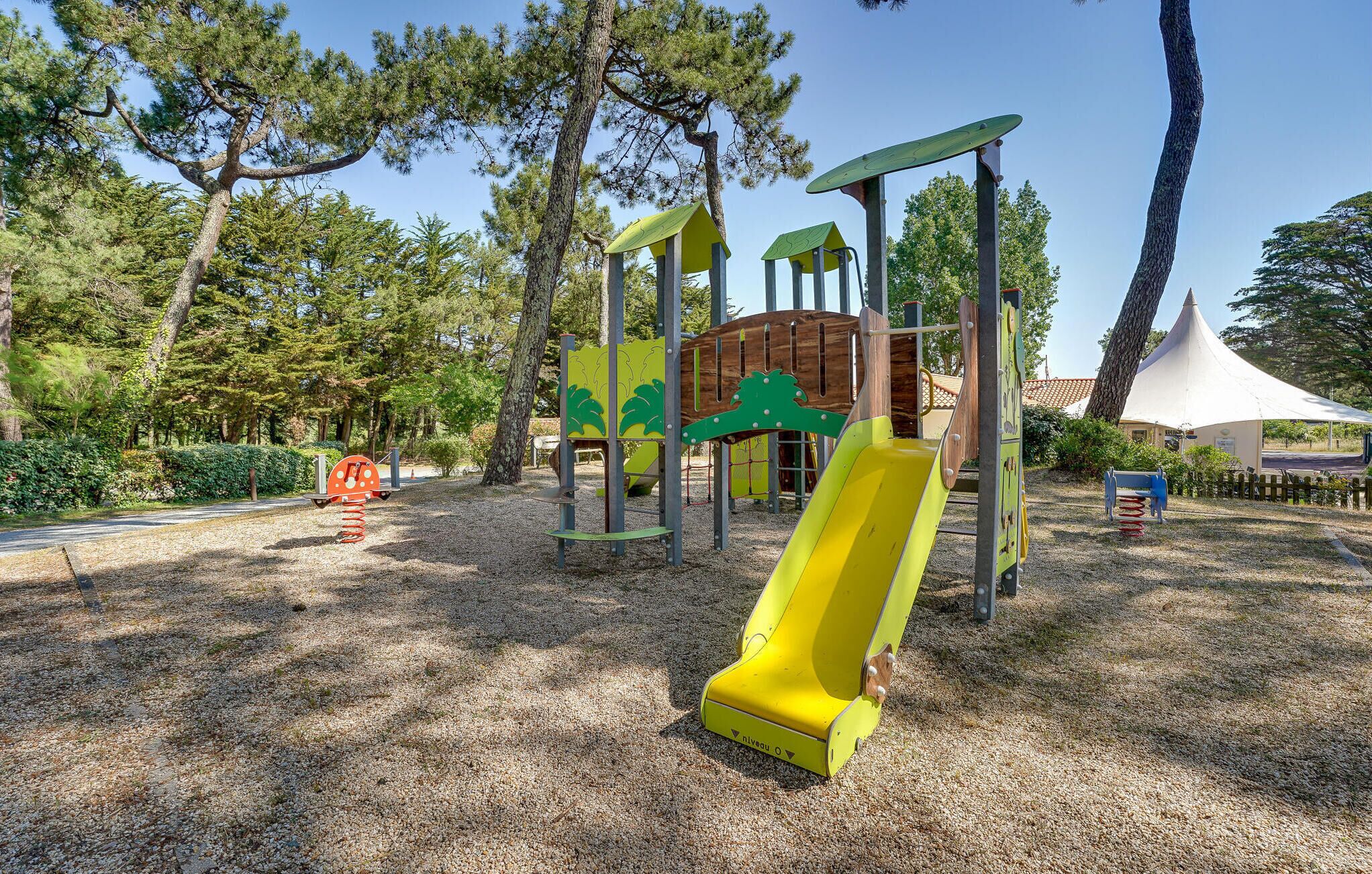 Um parquinho infantil com um escorrega amarelo, estruturas de escalada e uma casinha de madeira.
