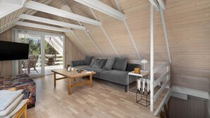 A cozy loft-style room with a wooden floor, a gray sofa, a wooden coffee table, and a TV mounted on the wall. - 3 bedroom cozy home in Højslev (Højslev)