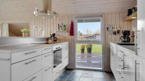 A modern kitchen with white cabinetry, a large island, and a view of the outdoors through a glass door. - Beautiful home in Sydals with WiFi (Sydals)