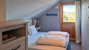 Une chambre à coucher comprenant un lit, une table de chevet, une lampe, une fenêtre avec des rideaux et une vue sur l’extérieur.