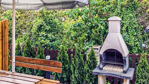 Um banco de madeira e um forno de pedra ao ar livre num jardim com cerca de madeira e vegetação exuberante.